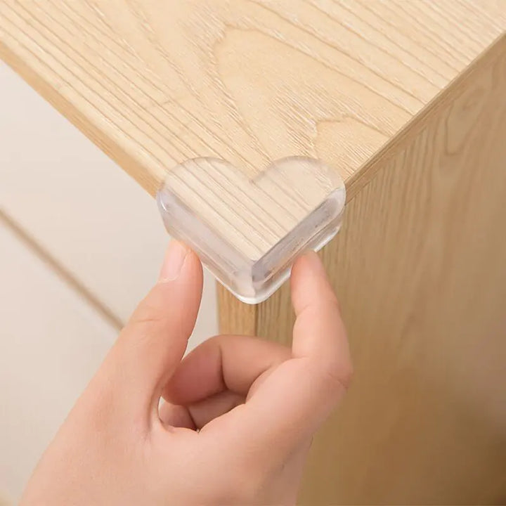 Clear plastic corner protector being held by a hand against a wooden surface