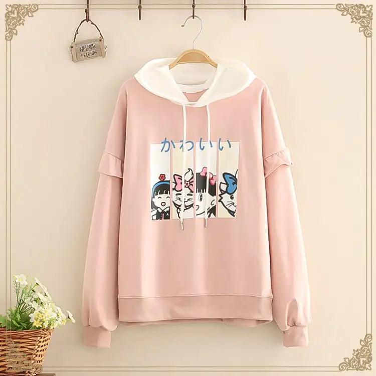 Pink hoodie with cartoon design on a hanger against a beige wall.