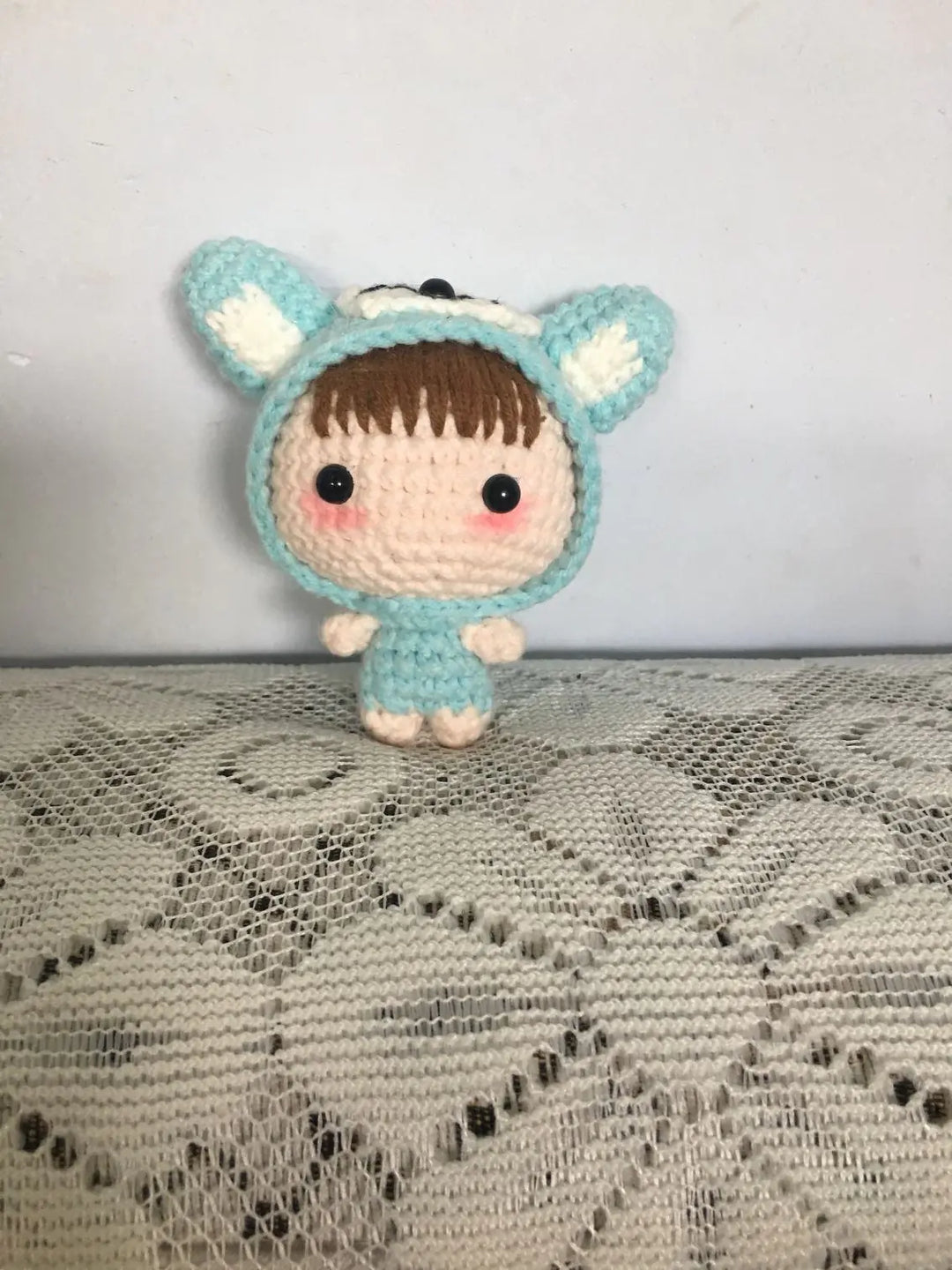 Crocheted toy with a blue hood and white accents on a textured surface
