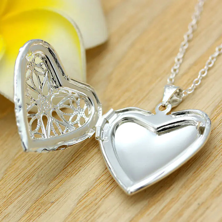 Silver heart-shaped locket on a wooden surface with a yellow flower in the background