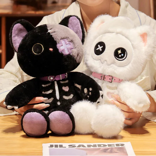 Two plush toys, one black and one white, held by a person on a wooden surface with a Jil Sander card in the foreground.