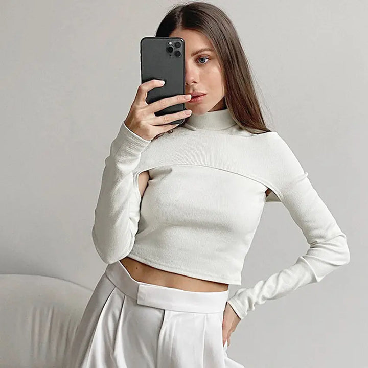Woman wearing a white long-sleeve top and pants, taking a mirror selfie.